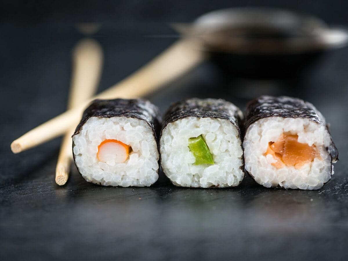 Drei Maki mit Lachs, Gurke und Omelett neben Essstäbchen, Kurs Asiatisches Fischkonfekt