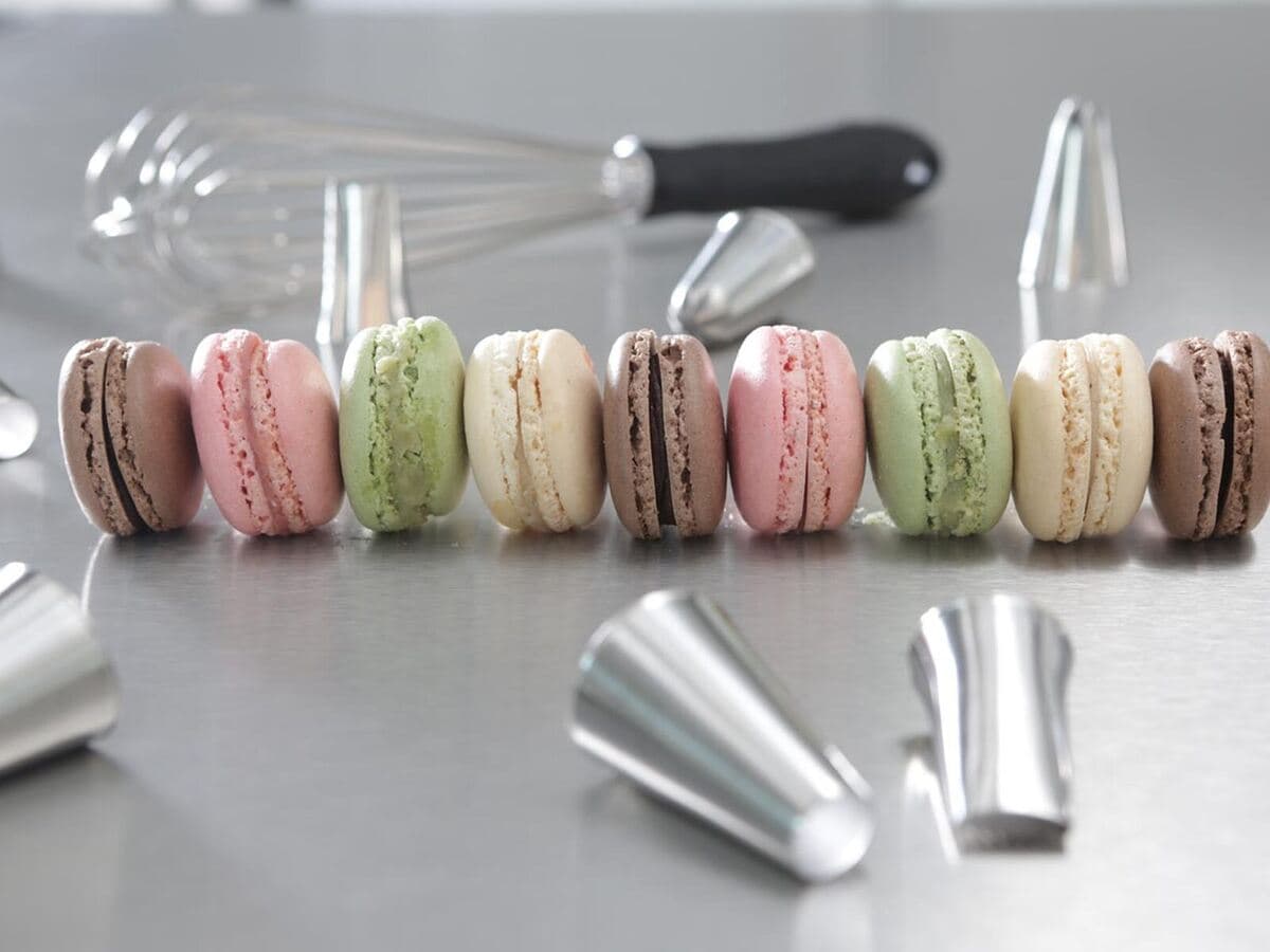 Bunte Macarons in einer Reihe neben Schneebesen und Spritztüllen, Kurs Frankreich’s kleine Sünde